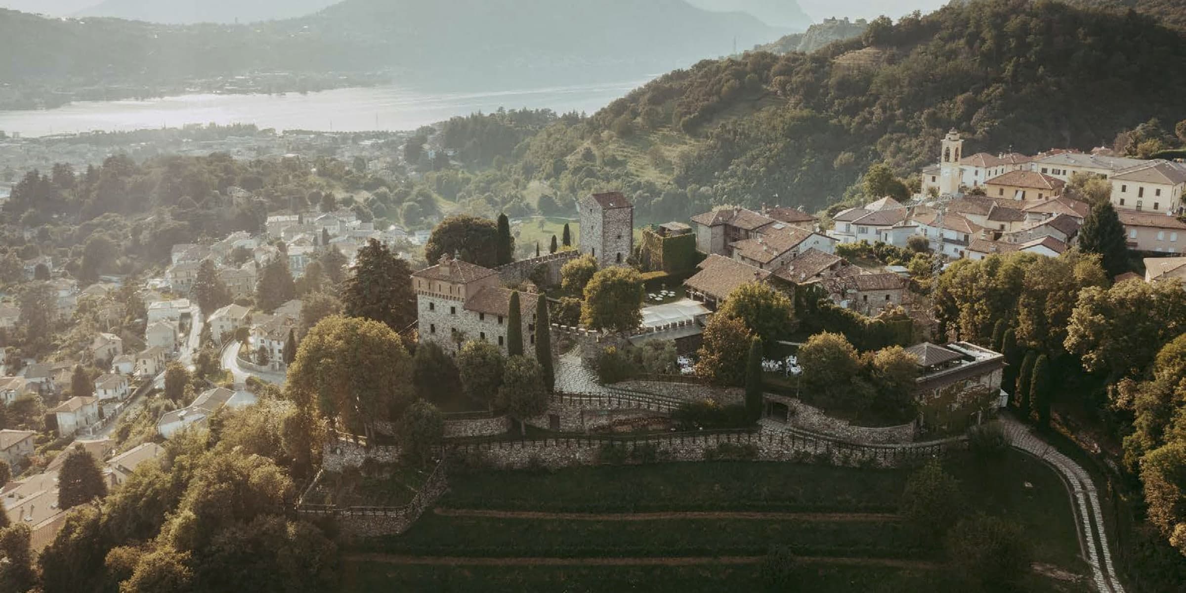Aerial view of Castello di Rossino above Lake Como, with the village of Calolziocorte and the lake misty in the distance